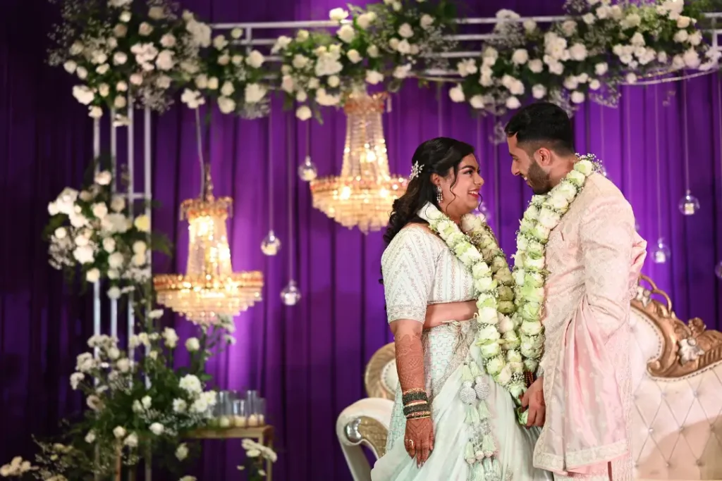 Couple exchanging wedding garlands on purple floral stage arranged by best wedding planning in Bangalore