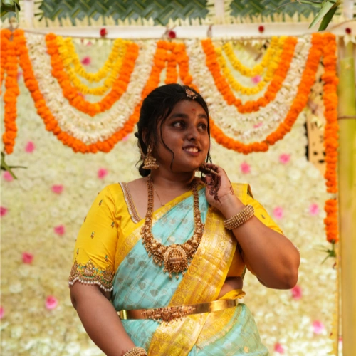 Bride in yellow and blue saree posing in front of vibrant marigold wedding decor